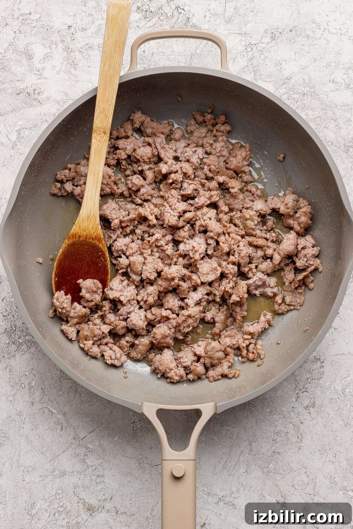 Cooked ground sausage in a skillet with a wooden spoon.