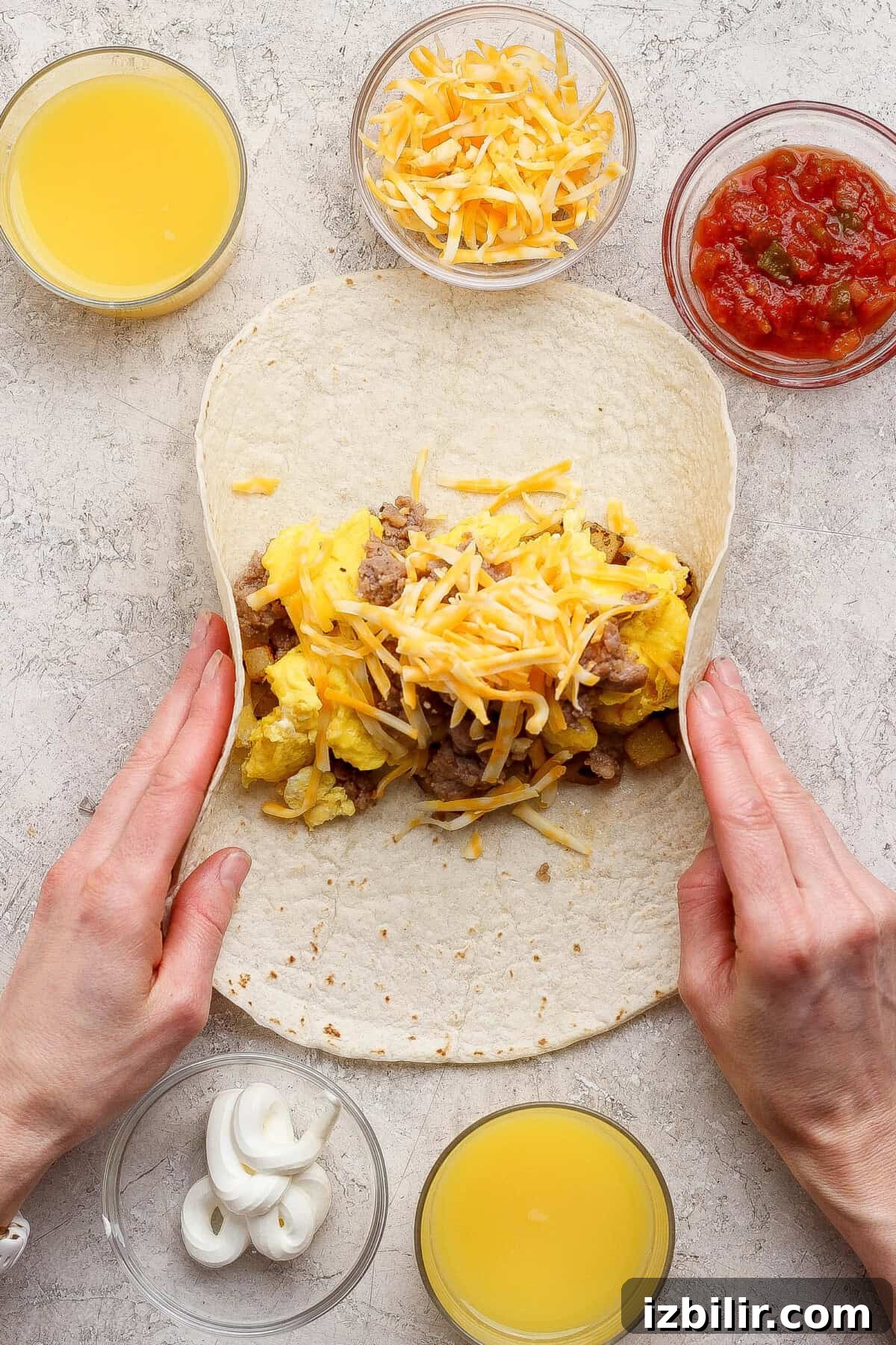 Hands rolling a tortilla filled with scrambled eggs, cheese, and meat.