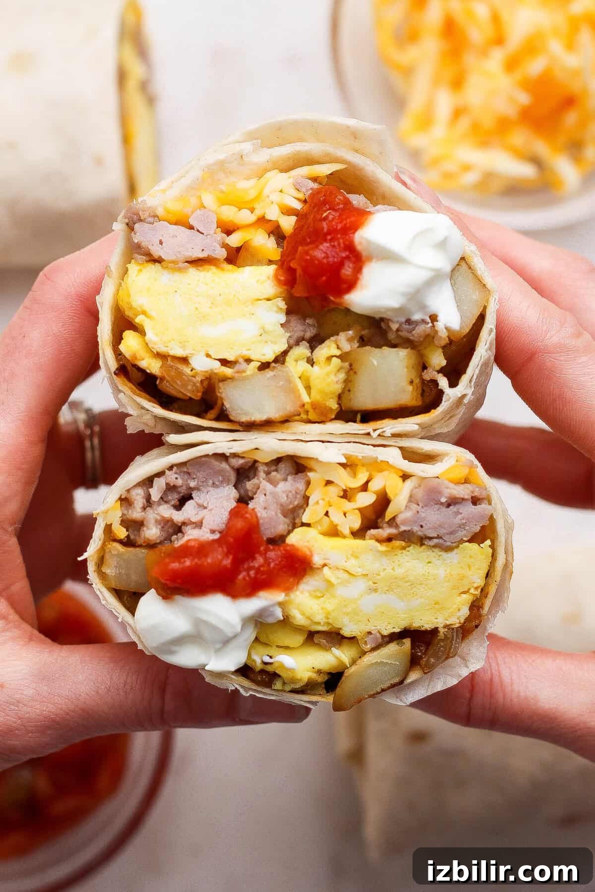 Halved breakfast burrito filled with scrambled eggs, sausage, potatoes, shredded cheese, salsa, and sour cream.
