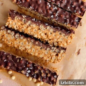 Four chocolate-covered, crispy peanut butter bars topped with sea salt, arranged on parchment paper.