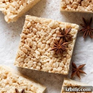 A square rice crispy treat topped with star anise spices, placed on a light-colored surface. Other identical treats and star anise pieces are shown around it.