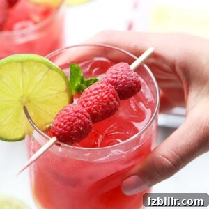 A person holding a raspberry mojito garnished with lime.