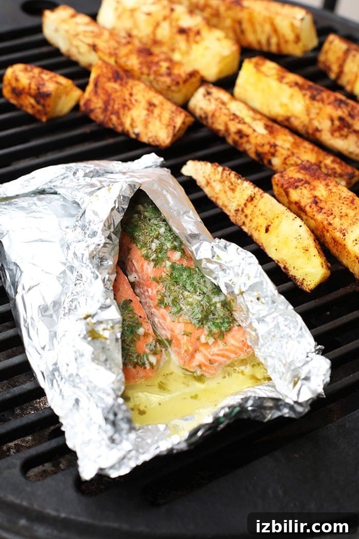 Salmon in a foil on the grill with pineapple next to it.