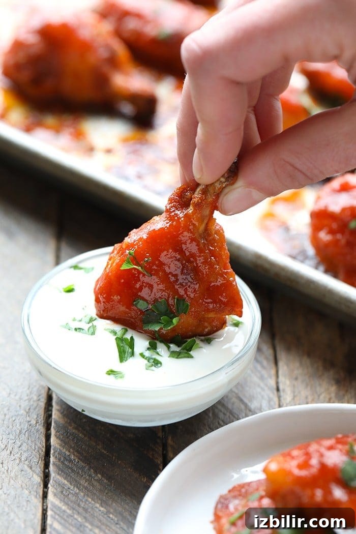 Crispy Baked Buffalo Chicken Wings Recipe 2 baked buffalo chicken wing being dipped in yogurt sauce