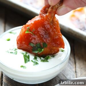 Crispy Baked Buffalo Chicken Wings Recipe 6 A person enjoying baked chicken wings by dipping them into a bowl of sauce.