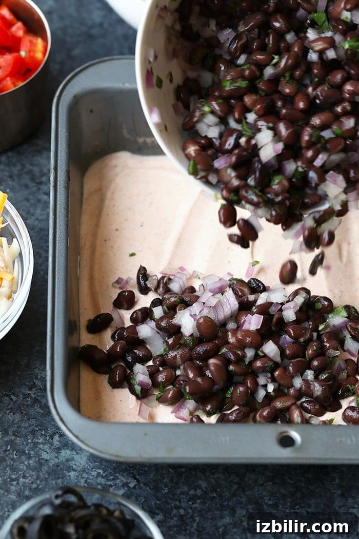 Adding black bean layer black bean layer of taco dip being poured into a pan