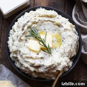 a bowl of healthy mashed potatoes with butter and a sprig of rosemary.