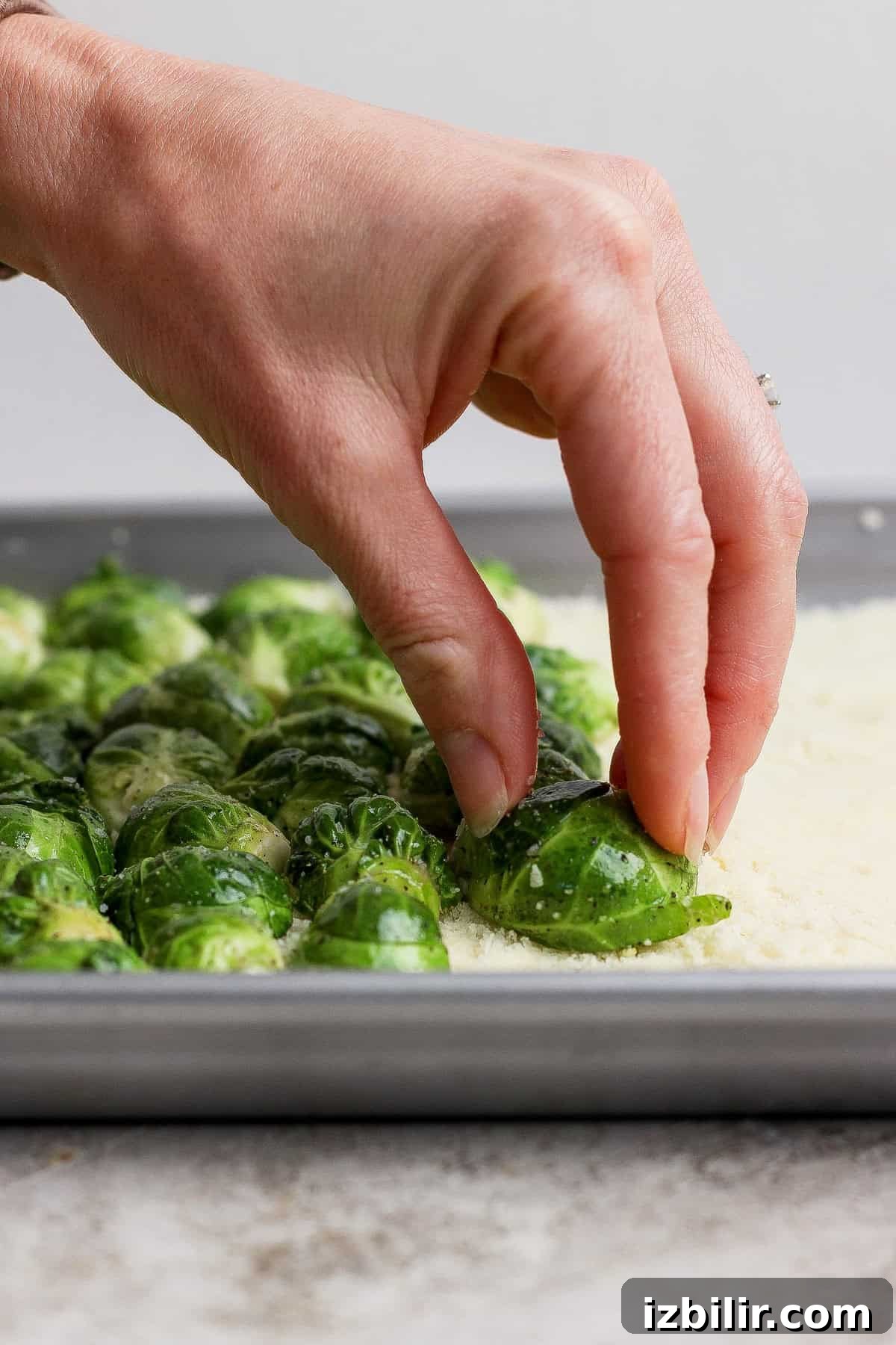 Crispy Parmesan-Crusted Brussels Sprouts Recipe 5 A hand presses a halved Brussels sprout into a layer of grated cheese or breadcrumbs on a baking sheet with more Brussels sprouts.