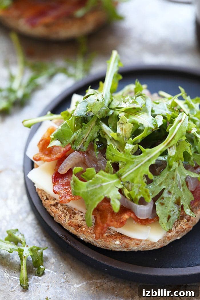Layered breakfast sandwich showing egg, arugula, cheddar, bacon and caramelized onions.