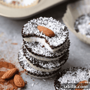 Homemade Almond Joy Cups Recipe 2 A stack of three Almond Joy Cups with a bite taken out, revealing layers of chocolate and coconut, topped with almonds.