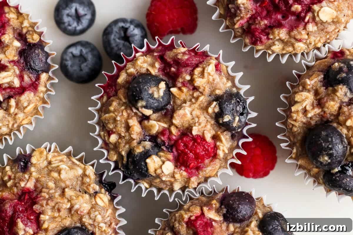 Baked oatmeal muffins topped with blueberries and raspberries, arranged on a white surface with additional berries nearby.