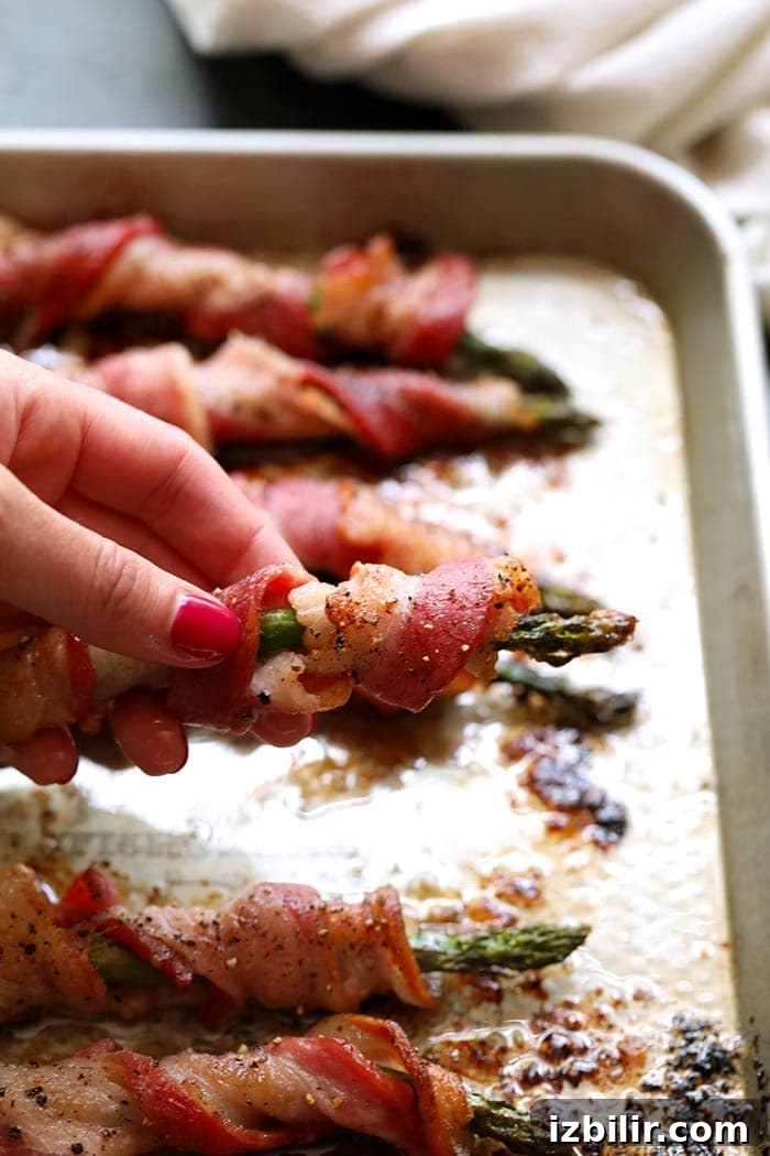 Everyone will love this bacon wrapped asparagus recipe! a hand holding bacon wrapped asparagus