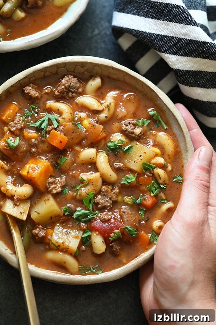 A hand holding a bowl of hamburger soup
