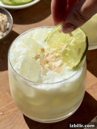 Boozy Coconut Brazilian Lemonade in a glass with lime garnish and toasted coconut