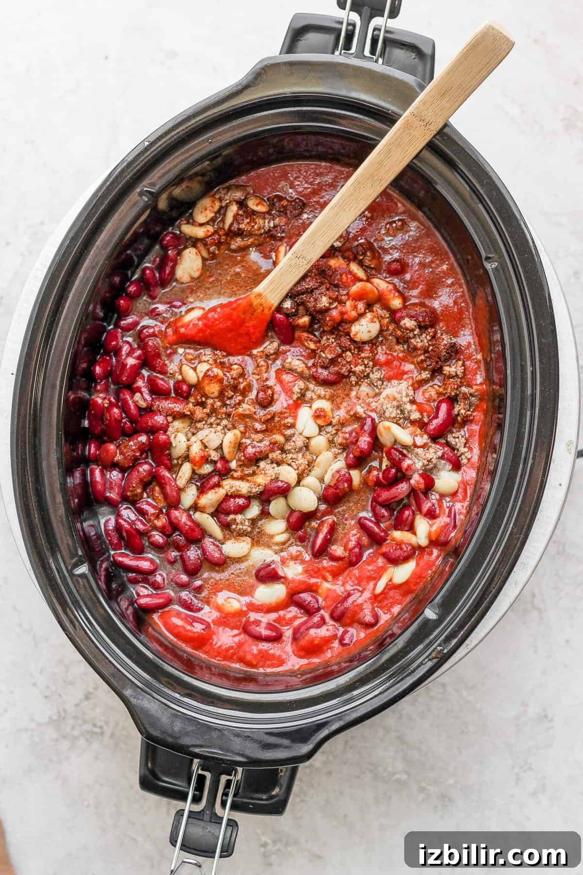A slow cooker turkey chili simmering with a wooden spoon.