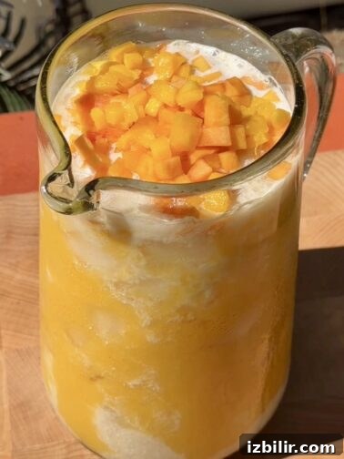 Creamy Mango Peach Agua Fresca in a pitcher with fruit chunks and ice