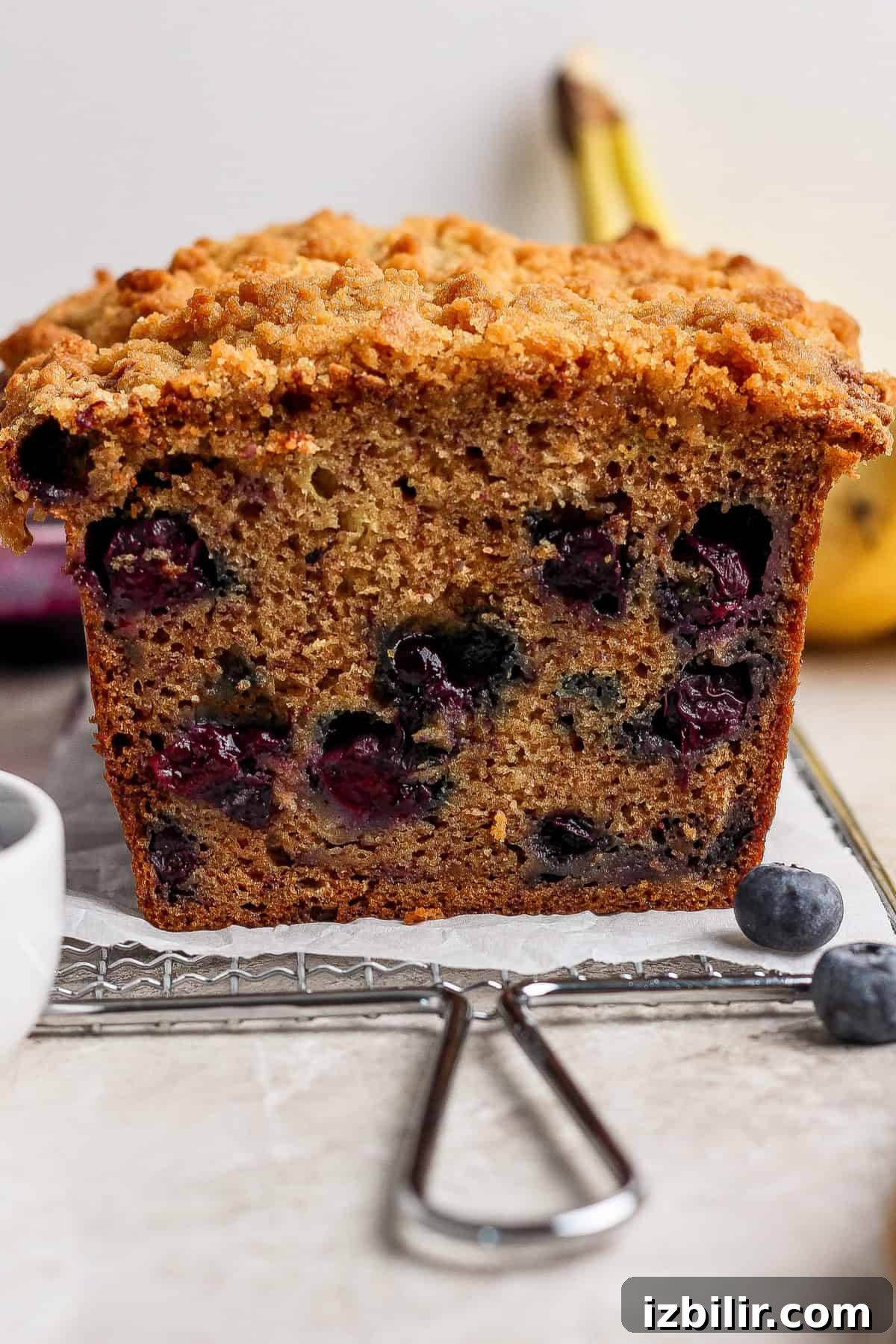 A close-up of a sliced loaf of blueberry banana bread with a crumb topping, showing blueberries inside the bread.