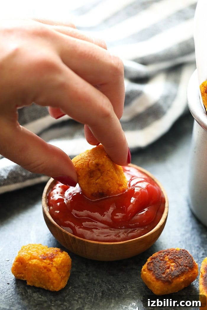 These healthy sweet potato tater tots are family-friendly and delicious A hand dipping a tater tot into ketchup.
