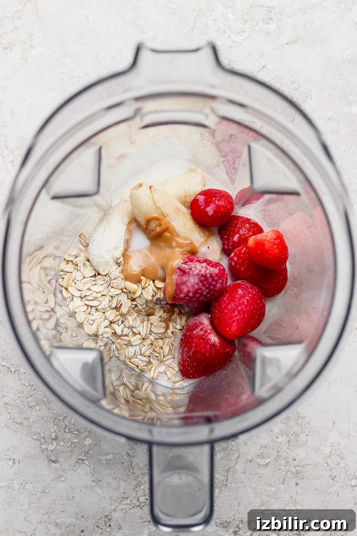 Oats, banana, frozen strawberries, peanut butter, and milk are placed in a blender, ready to be mixed.