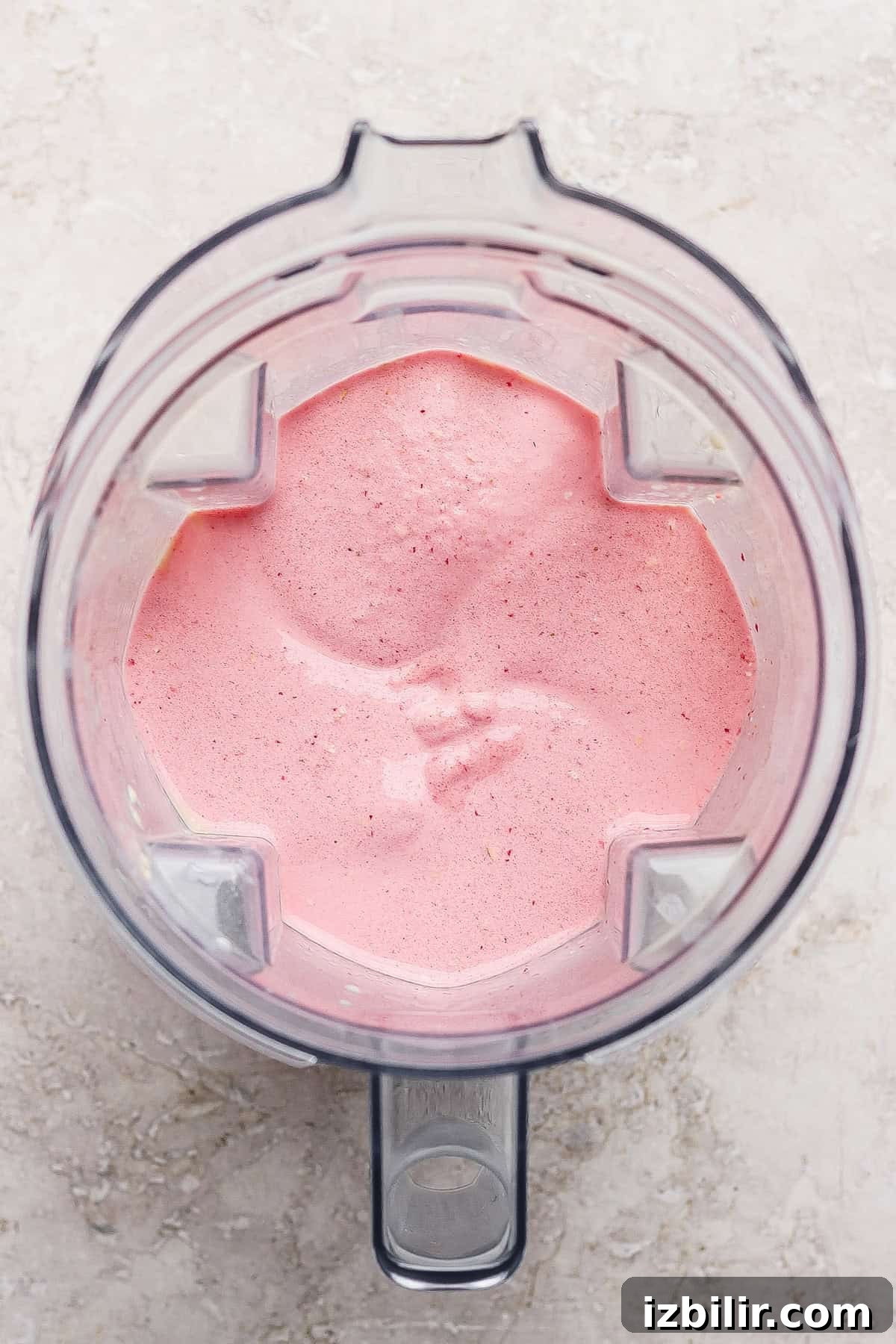A top-down view of a blender containing a thick, pink smoothie mixture on a light-colored countertop.