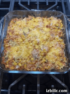 A glass baking dish filled with a chicken casserole featuring rice, corn, diced vegetables, and melted cheese on top