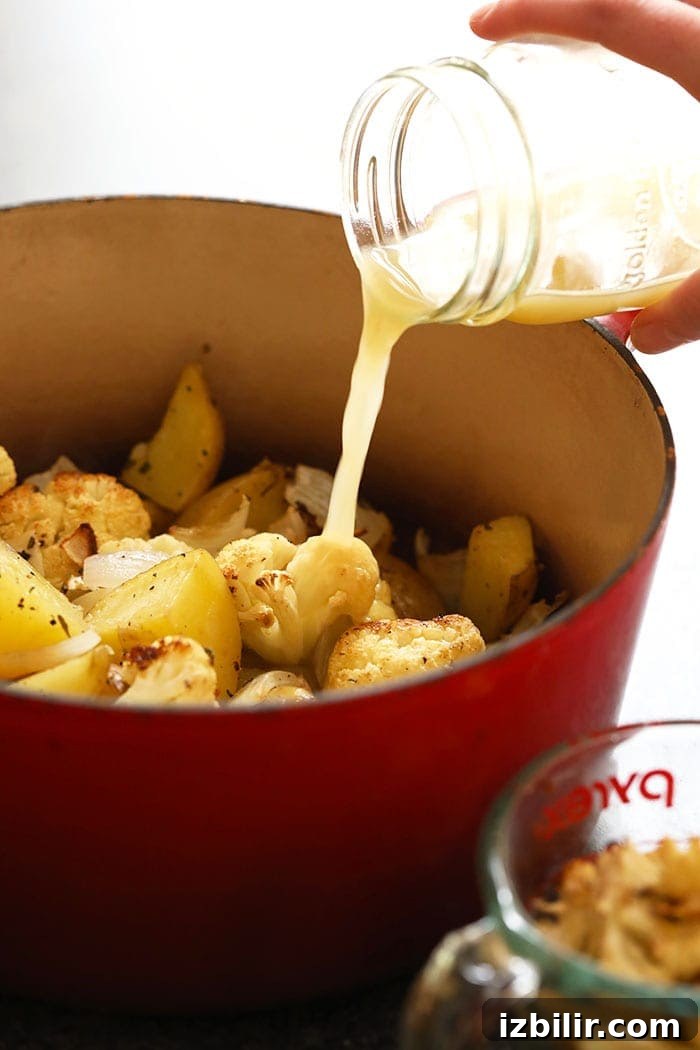 roasted potatoes and cauliflower with chicken broth being poured on it