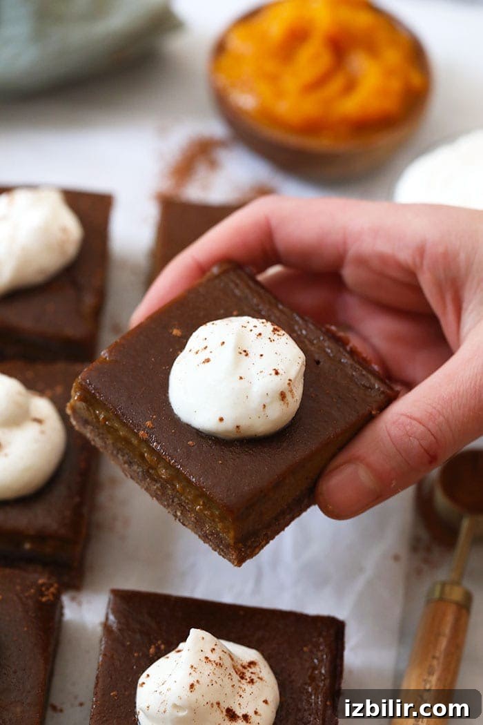 Pumpkin pie bar with whipped topping A hand holding a pumpkin pie bar with whipped cream topping