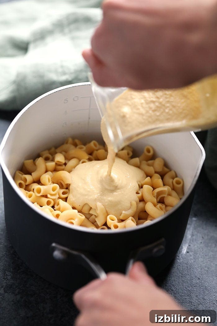 Pouring cashew cheese sauce over cooked pasta. vegan mac and cheese sauce being poured over noodles
