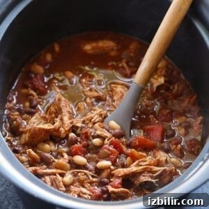 Crockpot chicken chili with a wooden spoon in it.