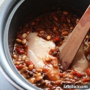 A crockpot full of chili and beans with a wooden spoon.