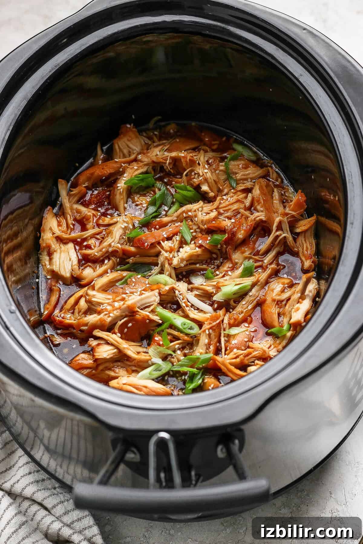 Sticky Honey Garlic Chicken Recipe 5 Closeup of shredded honey garlic chicken in a crockpot with sesame seeds and green onions