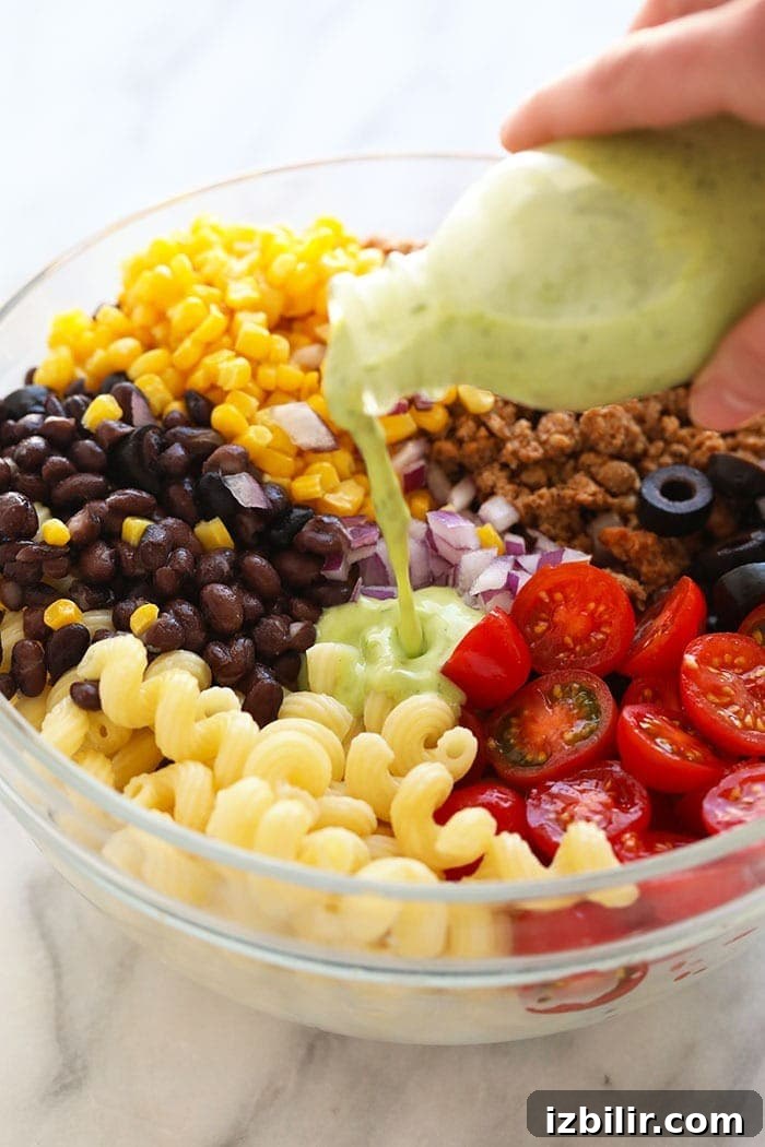 Taco Pasta Salad Recipe with Ground Beef, Cheddar and Corn 4 Pouring dressing on pasta salad.
