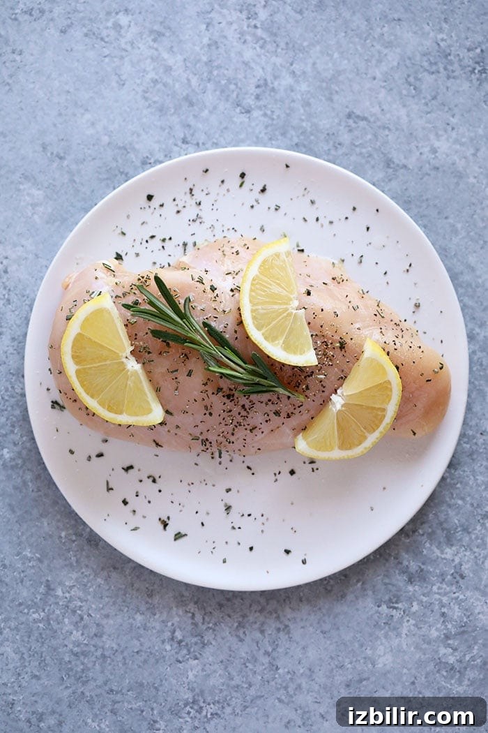 Raw chicken breast with lemon and rosemary raw chicken breast on a plate with lemons and rosemary.