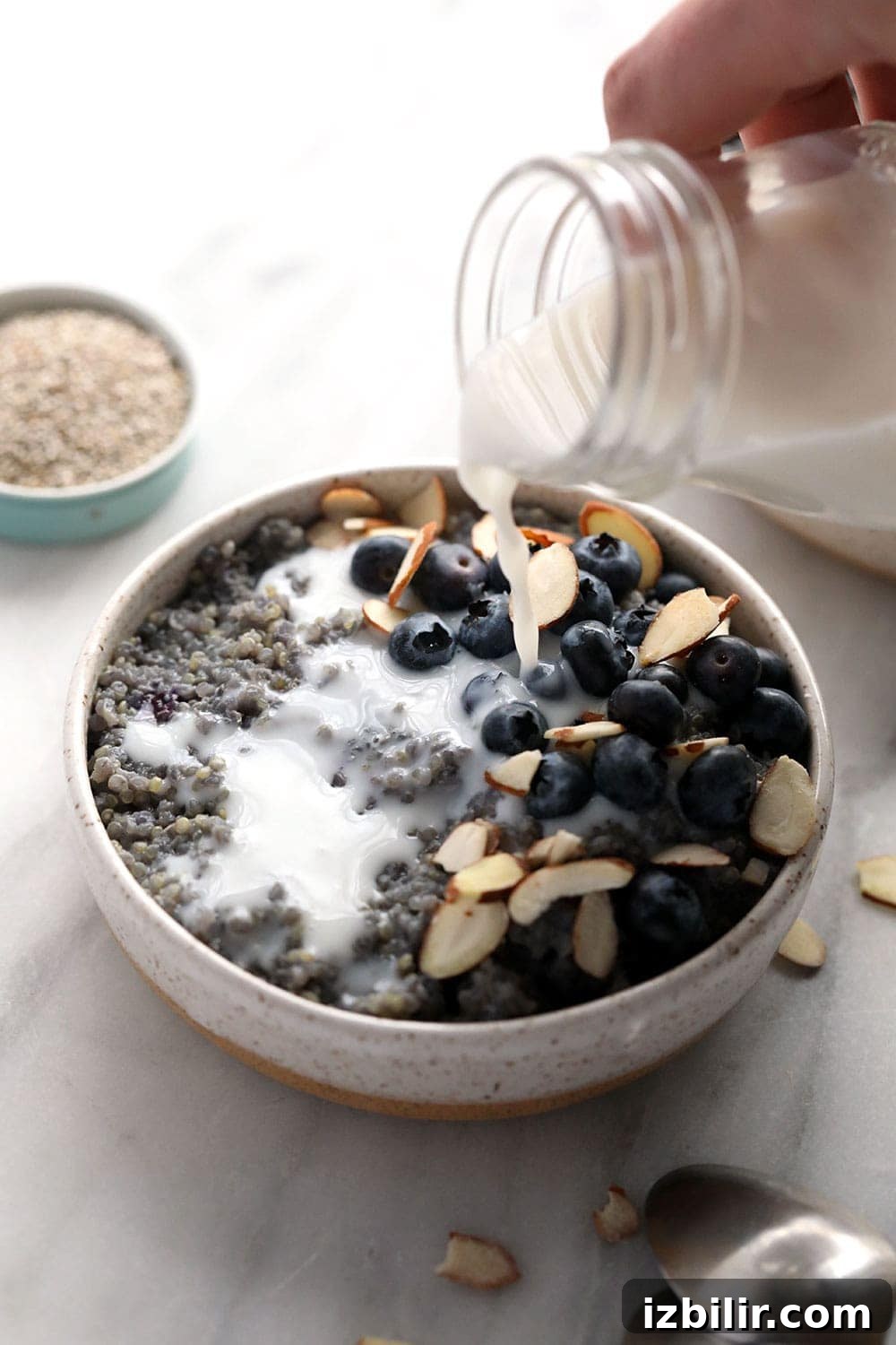 Pouring almond milk over blueberry breakfast quinoa. 