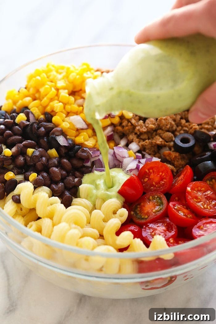 Pouring cilantro lime dressing into a pasta salad