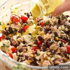 A hand pouring dressing into a glass bowl filled with fiesta tuna salad