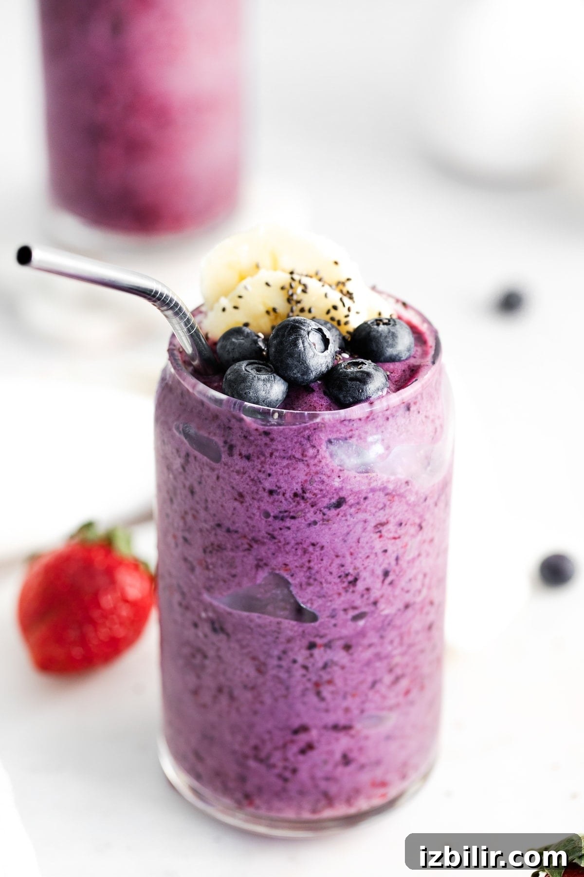 Triple Berry Protein Smoothie triple berry smoothie in a glass topped with fresh blueberries.