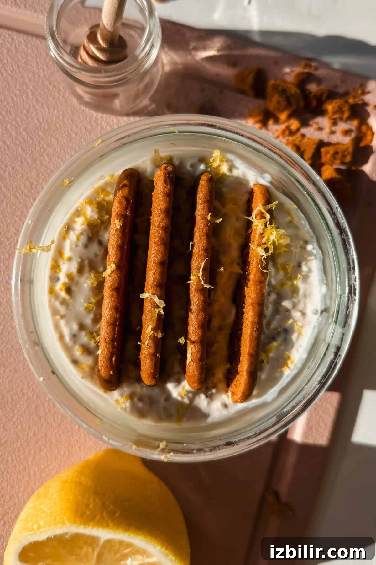 Creamy Lemon Cheesecake Overnight Oats Recipe 2 A glass jar of creamy overnight oats topped with cookies and lemon zest.