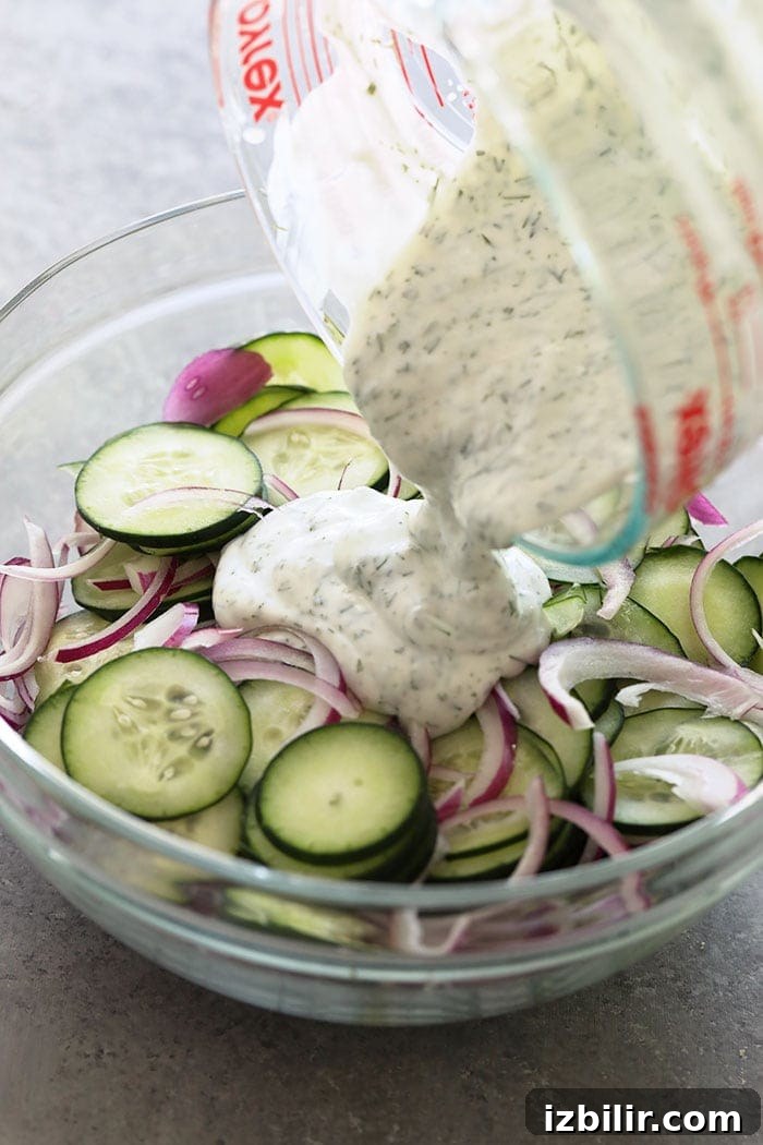 If you are looking for a healthy side salad for your next BBQ or a healthy salad for meal prep, look no further! This creamy cucumber salad is simple, flavorful, and delicious. Pouring dressing on cucumber salad.