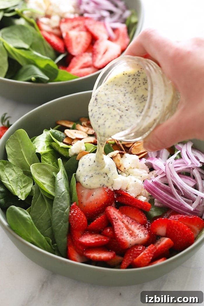 Pouring poppy seed dressing over a strawberry spinach salad.