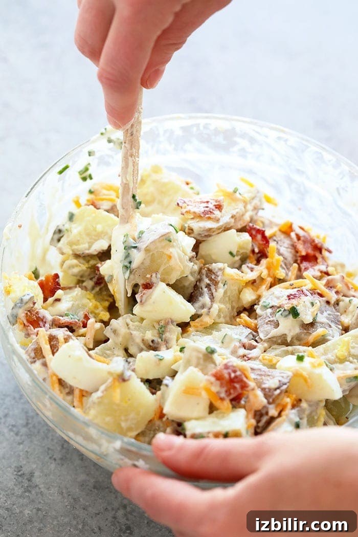 Hello, delicious and creamy loaded baked potato salad. This is the perfect hearty salad to serve at any summer BBQ. A hand mixing loaded baked potato salad