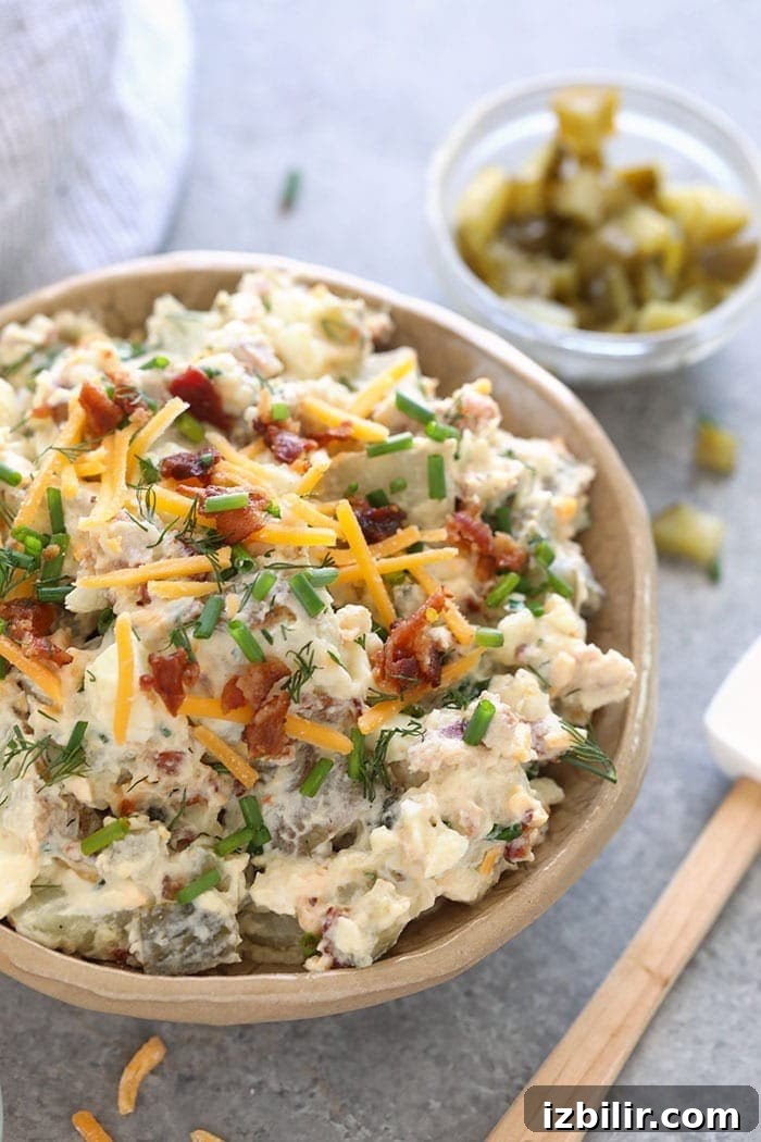 This baked potato salad recipe is loaded with cheddar cheese, hard boiled eggs, bacon, chives, and a delicious dill pickle sauce! loaded baked potato salad in a bowl