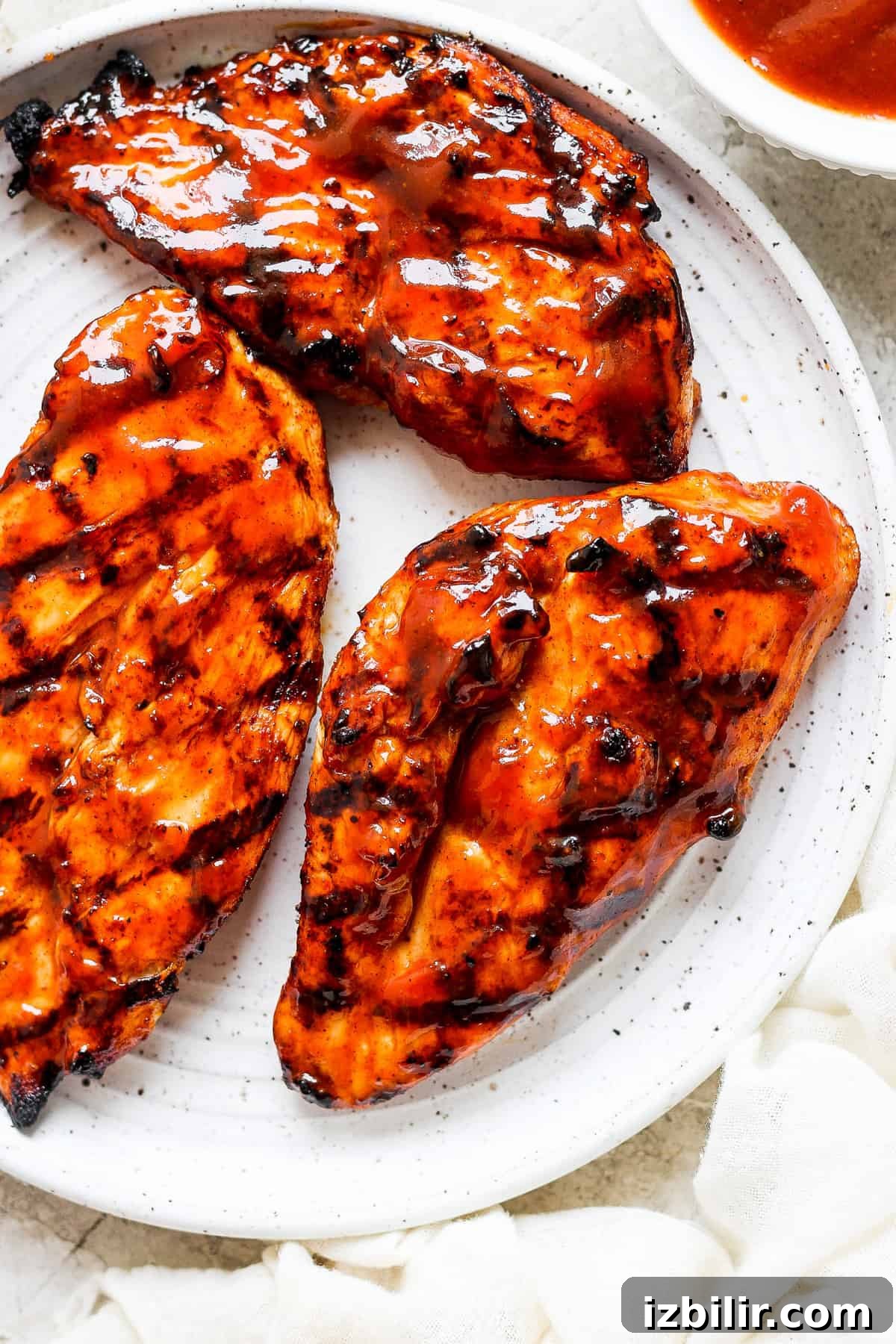 grilled chicken breasts on a white plate with sauce.