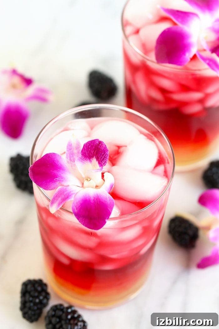 Hibiscus Arnold Palmer with edible flowers and blackberries arnold palmer drink in a glass with an edible flower surrounded by blackberries