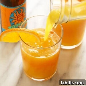 a glass of orange juice is being poured into a beermosa.