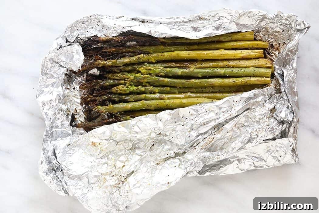 grilled asparagus in foil on a white plate with lemon wedges