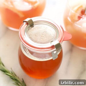 A glass jar with orange juice, honey simple syrup, and a rosemary sprig.