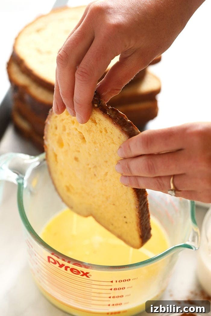 whole wheat bread being dipped in egg mixture for sheet pan french toast