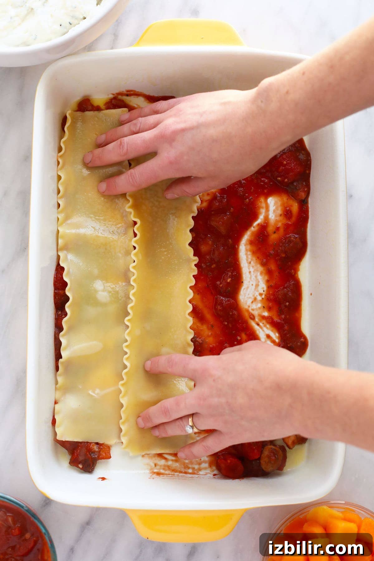 Hands placing lasagna noodles in a 9x13 casserole dish.
