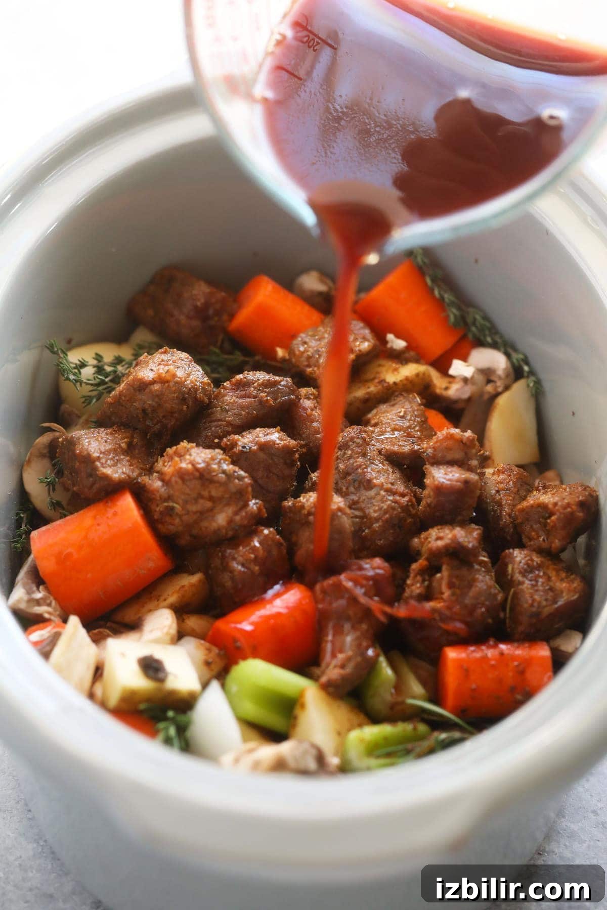 slow cooker beef stew ingredients being mixed together in a slow cooker